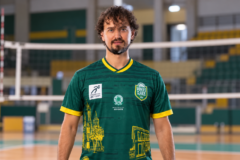 Vitinho Hillmann com uniforme verde do MOC Vôlei, em composição com ginásio de vôlei ao fundo.